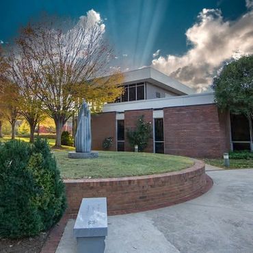 A modern brick building with a sculpture and autumn trees under dramatic sky.