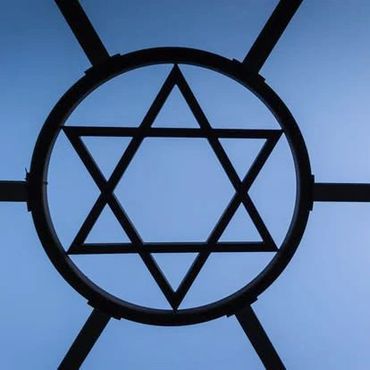 Star of David framed by a circular metal structure against a clear blue sky.