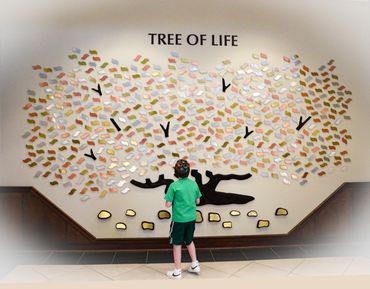 A boy stands in front of a colorful Tree of Life wall art installation.