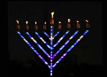 Illuminated menorah with eight lit candles against a dark night sky.
