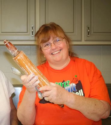 Smiling woman holding a flour-covered rolling pin in a kitchen.