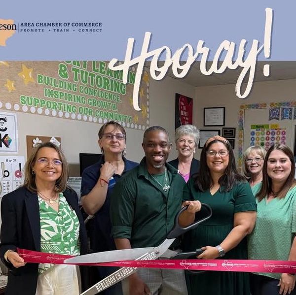 Group celebrates ribbon cutting with large scissors.