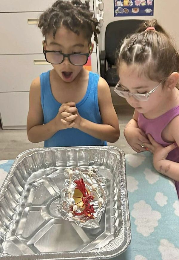 Two children with glasses excitedly looking at a foil tray with items inside.