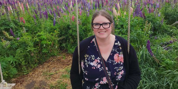 Woman smiling on a swing with purple flowers in the background.