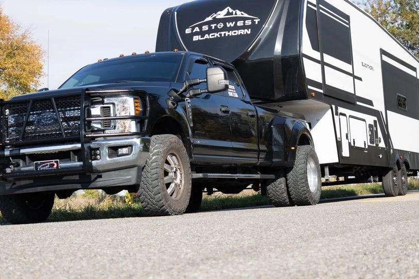 Black pickup truck towing a large white camper trailer.