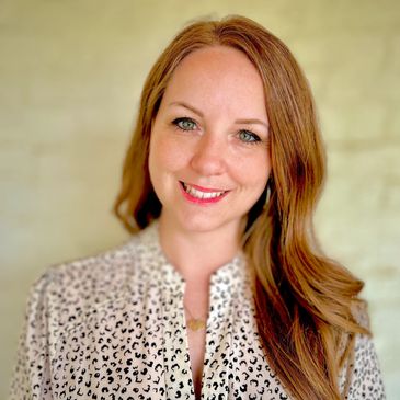 Smiling woman with long red hair and a patterned blouse.