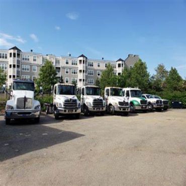 A row of six white trucks parked in front of an apartment building on a sunny day.