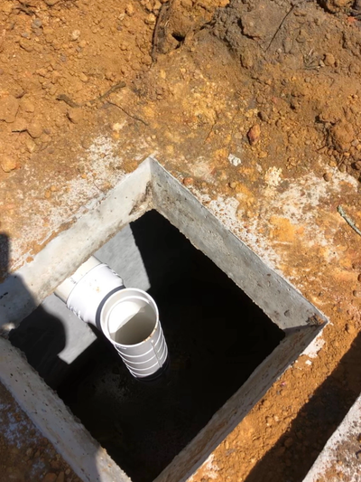 Concrete drainage pit with a white PVC pipe in soil.