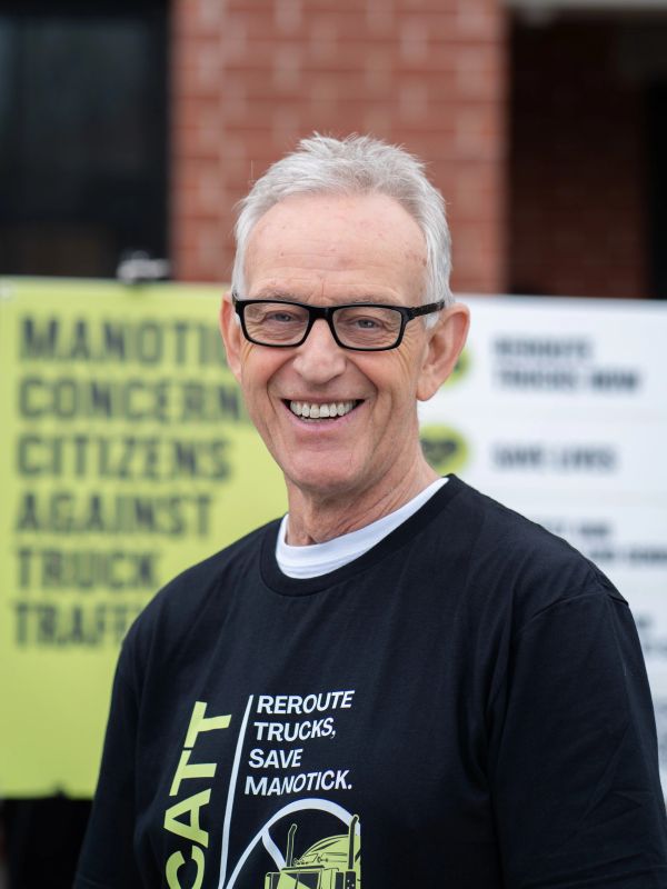 Smiling man wearing glasses and a protest shirt about truck traffic.