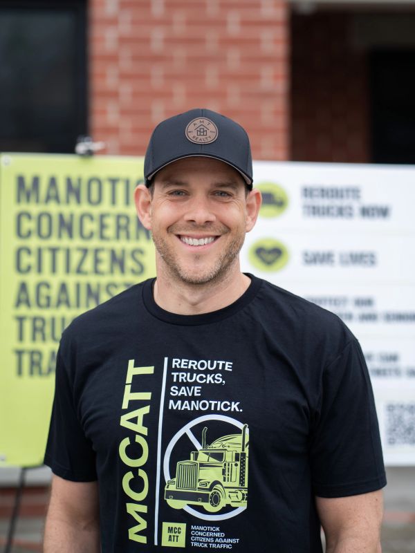 Man wearing a black cap and a protest T-shirt smiling outdoors.