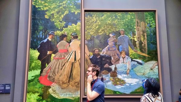 picture of a visitor walking past the CLaude Monet painting : Luncheon on the Grass in Orsay Museum