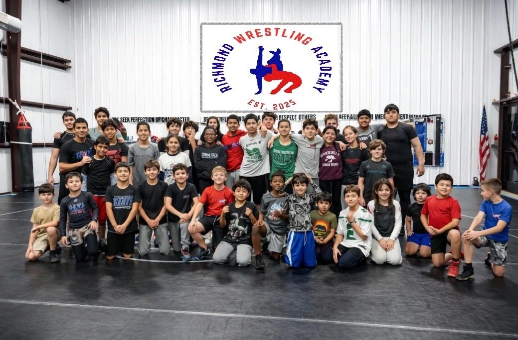 A large group of kids posing in a wrestling gym under a Richmond Wrestling Academy sign.