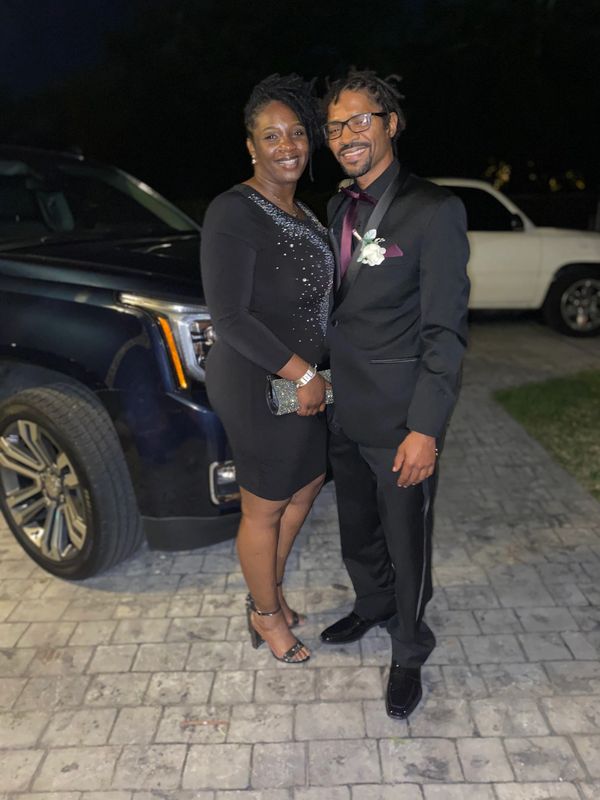 A couple dressed elegantly, smiling and posing outdoors at night.