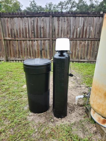 Black water softener system installed outdoors on grass.