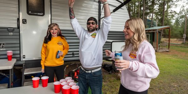 Three friends enjoy a game of beer pong outside a camper trailer.