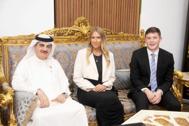 Three people sitting on an ornate gold and blue couch.