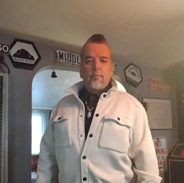 Man wearing a white jacket and a necklace indoors.