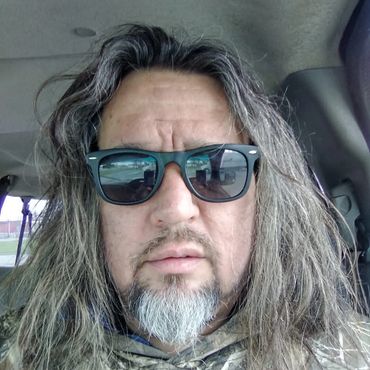 Man with long gray hair and beard wearing sunglasses inside a car.