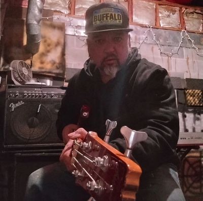 Man playing bass guitar in a dimly lit room with music equipment.