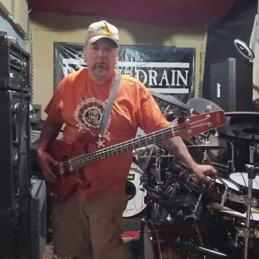Man in orange shirt playing bass guitar in a music rehearsal room.