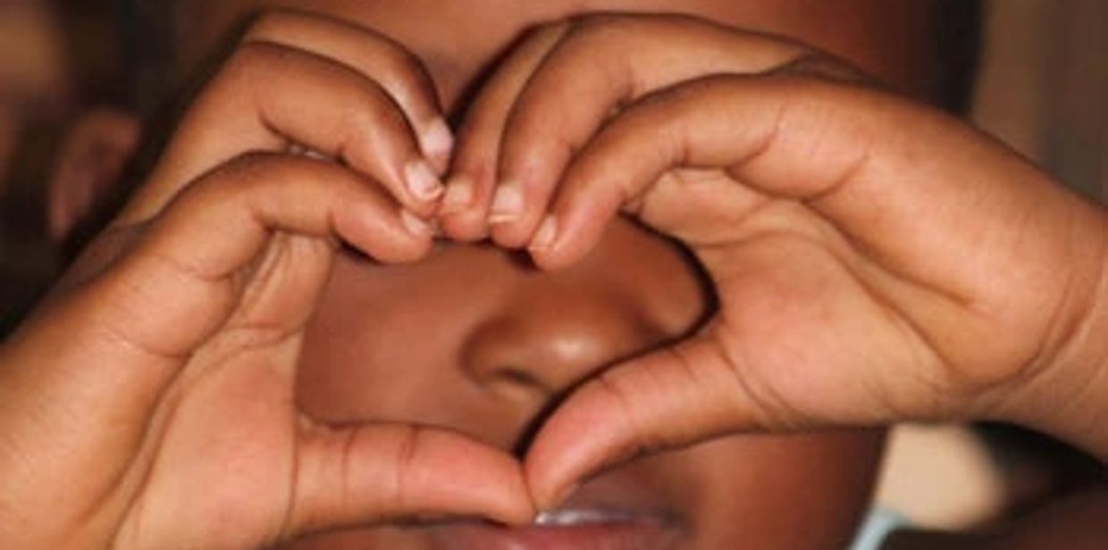 Child making a heart shape with their hands in front of their face.
