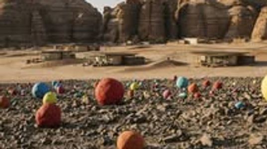 Colorful balls scattered on rocky ground with large stone structures in the background.