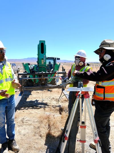 Construction workers discussing plans at a dry, desert job site with machinery.