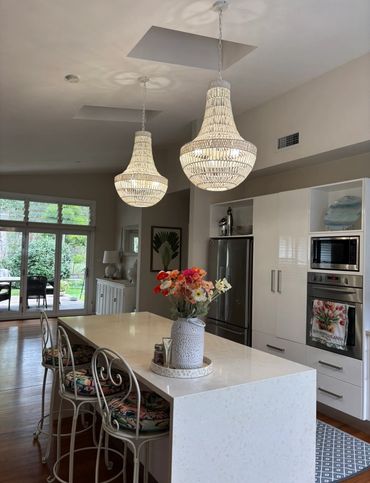 Modern kitchen with white island, floral cushions, and hanging chandeliers.