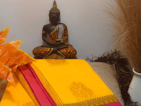 A Buddha statue with yellow cloth and autumn leaves beside it.