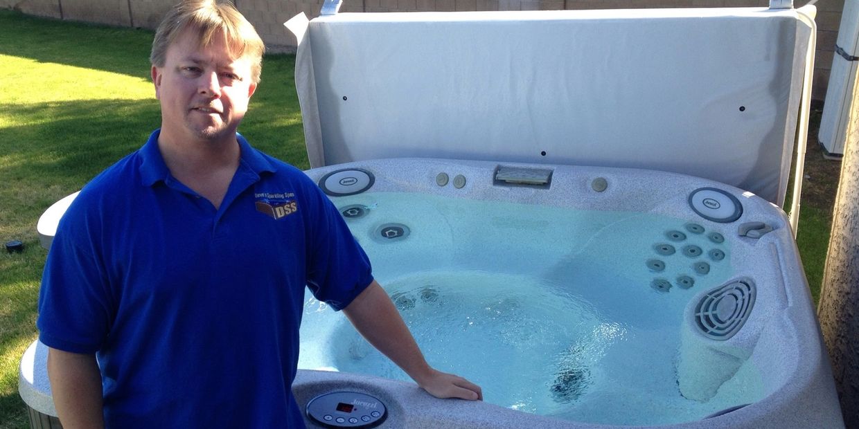 Man in a blue shirt stands beside a filled hot tub in a backyard.