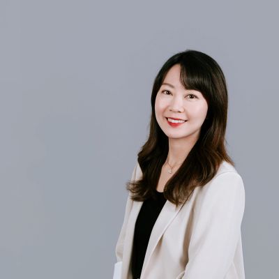 Professional woman smiling, wearing a white blazer against a grey background.