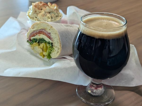 A sandwich, dip, and a dark beverage on a table.