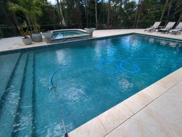 A clean pool with a vacuum hose and lounge chairs nearby.