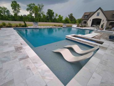Modern backyard pool with lounge chairs and fire feature near a house.
