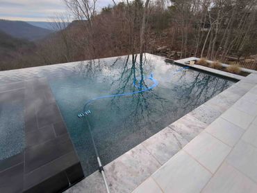A serene infinity pool overlooking a mountainous landscape with a pool vacuum cleaning.
