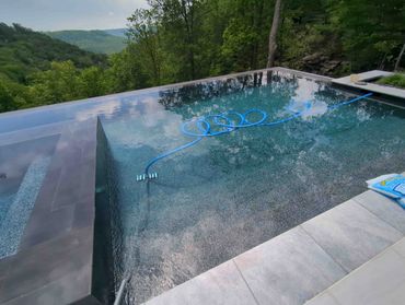 A serene infinity pool overlooking lush green mountains with a cleaning hose inside.