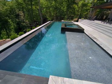 Modern rectangular pool with a built-in spa and surrounding forest.