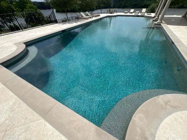 A clear blue swimming pool with lounge chairs by a lakeside.