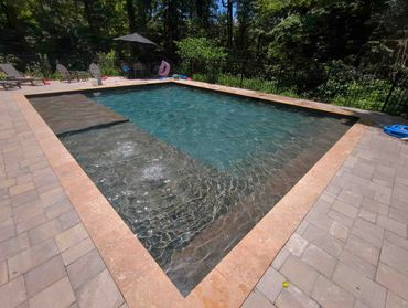 A clean outdoor pool surrounded by chairs and trees.