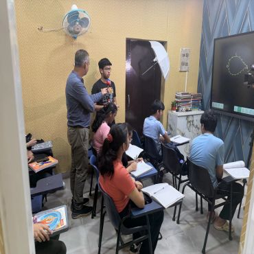 A classroom with students, an interviewer, and a whiteboard with a graph.