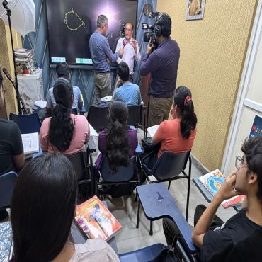 Classroom interview with students, camera crew, and a teacher explaining.