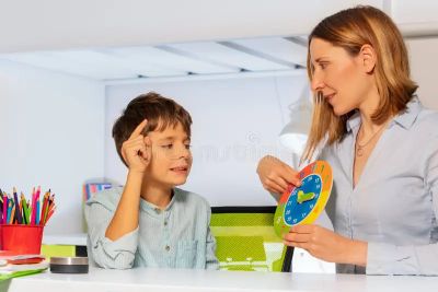 A woman teaching a boy to tell time using a colorful clock.