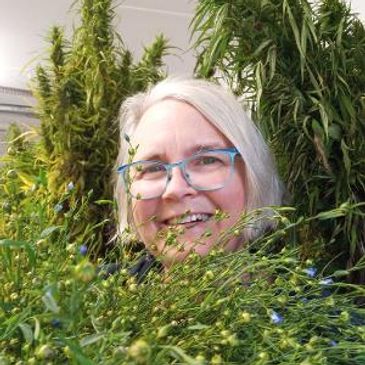 Smiling woman with glasses surrounded by lush green plants.