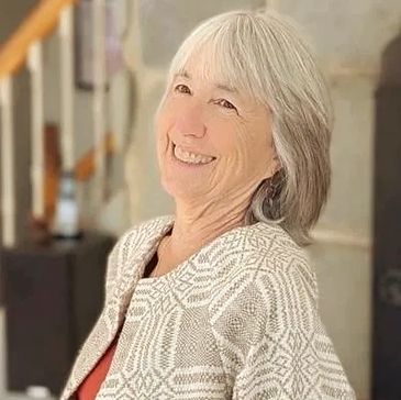 Smiling elderly woman with gray hair wearing a patterned sweater.