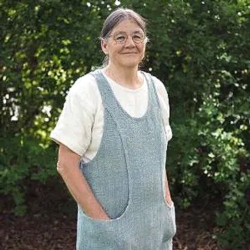 Smiling woman wearing glasses and blue overalls outdoors.
