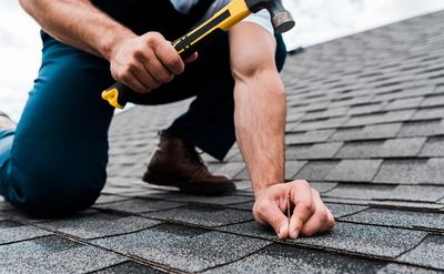 Roofer installing new gray asphalt shingles with a hammer during a roof replacement project.