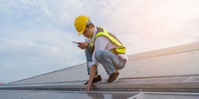 Professional solar installer wearing a hard hat and safety vest, inspecting a newly installed solar panel array on a rooftop.