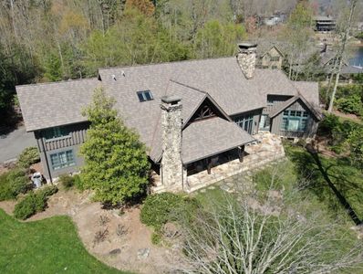 Aerial view of a custom home with a multi-gabled brown roof in wooded landscape