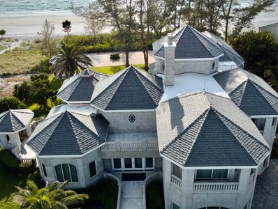 Aerial view of a luxury beachfront mansion with a complex synthetic slate roof design
