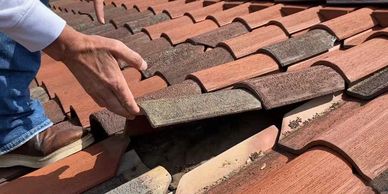 Roofer inspecting and lifting red tile to reveal worn out underlayment underneath